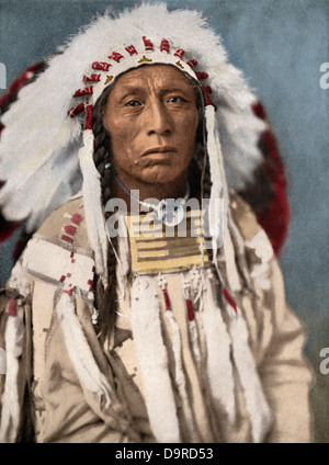 Crow Indian chief in una guerra tradizionale cofano e abbigliamento, circa 1900. Colorate a mano i mezzitoni di una fotografia Foto Stock