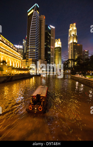 Il Cavenagh Bridge, una barca sul fiume Singapore, il Fullerton Hotel e il quartiere centrale degli affari di notte, Singapore Foto Stock
