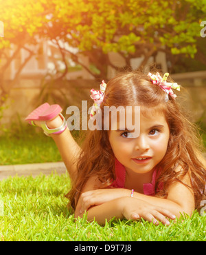 Closeup ritratto di carino arabo bambina sdraiati sull'erba verde campo sul cortile, lo stile di vita spensierata, infanzia felice Foto Stock