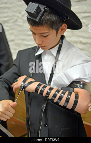 Giovane ebreo religioso ragazzo mette su phylacteries - tefillin - per la prima volta in una sinagoga a Brooklyn, New York Foto Stock