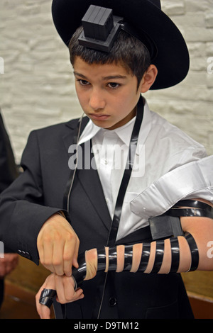 I giovani religiosi ragazzo ebreo mette su phylacteries - teffilin - per la prima volta presso la sinagoga Lubavitch a Brooklyn, New York Foto Stock