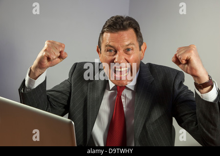 Ritratto uomo d affari a una scrivania cercando di fotocamera, il tifo con rinserrata pugni, seduto davanti a un computer portatile. Foto Stock
