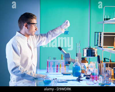 Vista laterale del farmacista in un laboratorio in possesso di una bottiglia di chimica con sostanza blu in esso Foto Stock