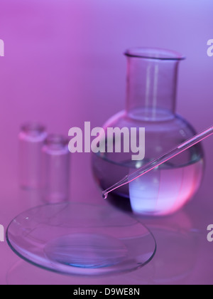 La caduta di pipetta di un liquido trasparente in un piatto con due bicchieri vuoti e un turno pallone con liquido trasparente nel Foto Stock