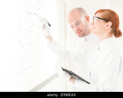 Due scienziati in un laboratorio avente una discussione e una condivisione di dati come la donna traccia diagrammi su un vetro o la scheda di interfaccia con un pennarello Foto Stock