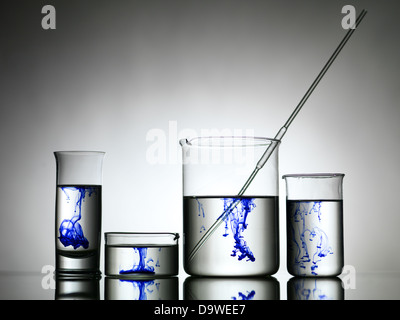 Grely gradiente dello sfondo con quattro diverse dimensioni bicchieri riempiti con soluzione incolore e colorante blu sgocciolato in loro Foto Stock