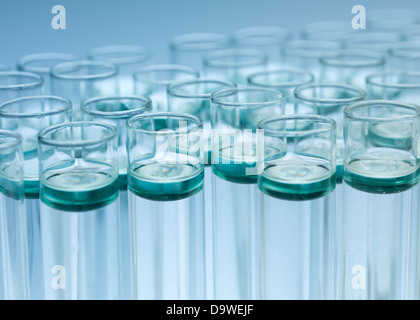 Luce di sfondo blu con una chiusura di una serie di test di laboratorio-tubi con soluzione incolore che è verde e toni di blu sulla superficie Foto Stock