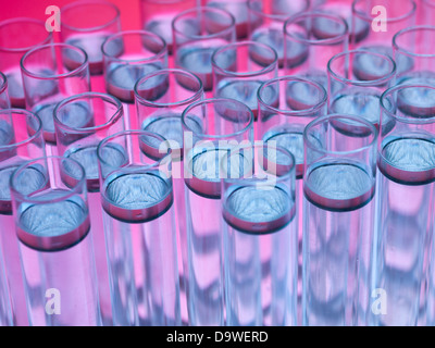 Vista aerea, macro di provette riempite con trasparente scuro sostanza galleggiante nel liquido incolore, contro un gradiente di colore rosa e sfondo viola Foto Stock