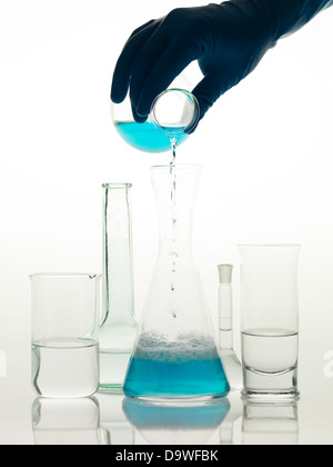 Vista frontale di diversi tipi di contenitori di vetro utilizzati in laboratorio, riempito con trasparente liquido incolore e uno in cui qualcuno è il versamento di un liquido di colore blu Foto Stock