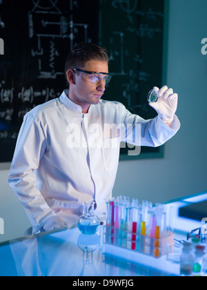 Maschio caucasico scienziato vestito di bianco uniforme studiando una capsula di petri con il campione, in un laboratorio Foto Stock