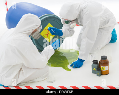 Close-up di due specialisti la raccolta di campioni da una pozza di rifiuti tossici liquidi indossando tute di protezione e maschere Foto Stock