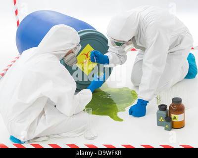 Close-up di due specialisti la raccolta di campioni da una pozza di rifiuti tossici liquidi indossando tute di protezione e maschere Foto Stock