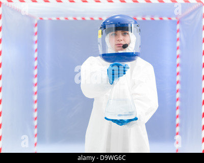 Fotografia di una donna scienziato indossare tuta protettiva e portante un barattolo di liquido tossico all'interno di un area di rischio biologico. Foto Stock