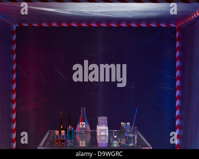 Diversi contenitori di vetro riempito con differenti liquidi colorati su un tavolo di vetro in una tenda di contenimento, posto all'esterno di notte Foto Stock