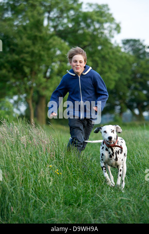 Giovane ragazzo insegue il suo gatto cane dalmata attraverso i campi di erba lunga. Foto Stock