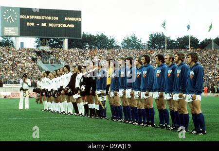 La nazionale di calcio delle squadre di Est e Germania Ovest stand in file per inni nazionali prima di iniziare il 1974 World Cup Soccer Game Germania Est contro la Germania ovest di Amburgo, Germania, 22 giugno 1974. La Germania occidentale, da L: centrocampista Uli Hoeness, defender Paul Breitner, difensore Berti Vogts, avanti Juergen Grabowski, centrocampista Wolfgang Overath, avanti Gerd Mueller, avanti Heinz Flohe, defender Georg Schwarzenbeck, defender Bernd Cullmann, portiere Sepp Maier, defender Franz Beckenbauer, arbitro uruguayano Ramon Barretto Ruiz (con sfera nelle sue mani). La Germania est, da L: defe Foto Stock