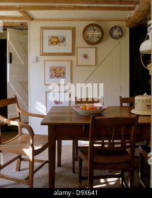 Rovere antico tavolo e sedie di legno in semplici cottage sala da pranzo con un visualizzatore di immagini sulla parete con orologio circolare Foto Stock