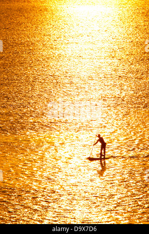 L'uomo paddleboarding in acque aperte al tramonto Foto Stock