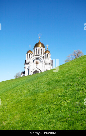 Bianco Chiesa Ortodossa con golden shining cupole sulla collina verde sopra il cielo blu Foto Stock