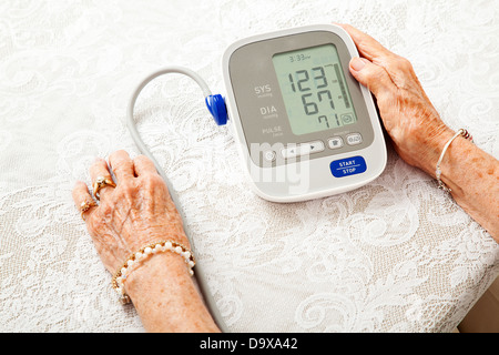 Primo piano di una donna senior le mani controllare la sua pressione del sangue su di un misuratore domestico. I risultati sono basse. Foto Stock