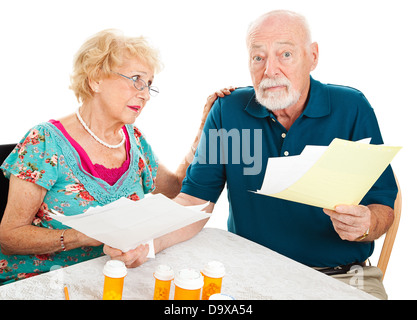 Coppia senior andando oltre le loro fatture mediche. Essi sono confusi e sopraffatti. Sfondo bianco. Foto Stock