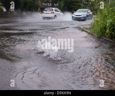 Cars driving attraverso strade allagate causato da burst acqua principali Foto Stock