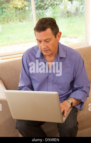 Buona ricerca uomo di mezza età seduto su un divano con un notebook. Foto Stock