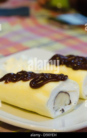 Close up crêpe rotoli riempiti con crema bianca e banana, topping con lo sciroppo al cioccolato , servita sul piatto bianco Foto Stock