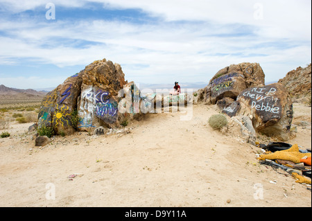 Ragazza adolescente in 'OBAY' cap seduti sulla coperta di graffiti rocce nel deserto di Mojave, California, Stati Uniti d'America. Foto Stock