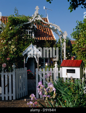 Arco in legno sopra cancello bianco in Picket Fence con postbox bianco nella parte anteriore del cottage del paese con portico bianco e il tetto di tegole rosse e Foto Stock