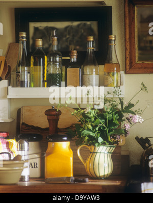 Close-up di bottiglie di una varietà di oli sul ripiano al di sopra di un vaso di fiori d'estate sul cottage piano cucina Foto Stock