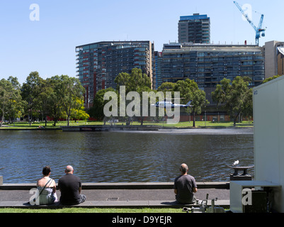 Dh Fiume Yarra Melbourne Australia gente seduta a guardare l'elicottero in arrivo Banca Yarra eliporto riverside Foto Stock