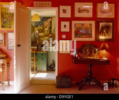 Raccolta di foto sulla parete sopra piccolo tavolo antico con la lampada accesa in rosso brillante cottage sala da pranzo Foto Stock