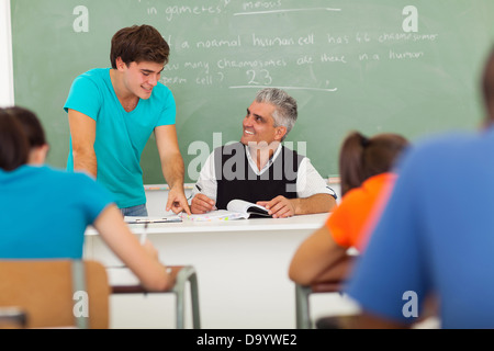 Gentile senior high school insegnante aiutare uno studente con il lavoro in classe Foto Stock