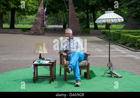 Adulto Uomo pensare e seduti su una sedia in un parco con tavolo e lampada Foto Stock