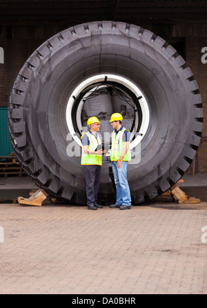 Allegro magazzinieri in piedi di fronte a un enorme pneumatico Foto Stock