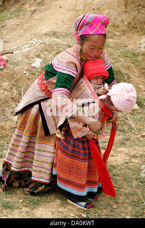 Fiore donna Hmong aiutare la propria figlia per ottenere il suo fratello sul retro al mercato di Bac Ha, Vietnam, sud-est asiatico Foto Stock