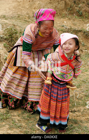 Fiore donna Hmong aiutare la propria figlia per ottenere il suo fratello sul retro al mercato di Bac Ha, Vietnam, sud-est asiatico Foto Stock