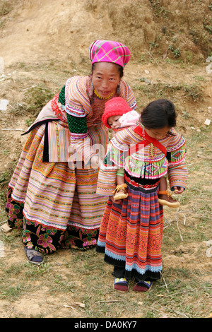 Fiore donna Hmong aiutare la propria figlia per ottenere il suo fratello sul retro al mercato di Bac Ha, Vietnam, sud-est asiatico Foto Stock