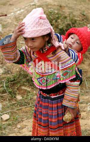 Fiore ragazza Hmong con suo fratello sul retro al mercato di Bac Ha, Vietnam, sud-est asiatico Foto Stock