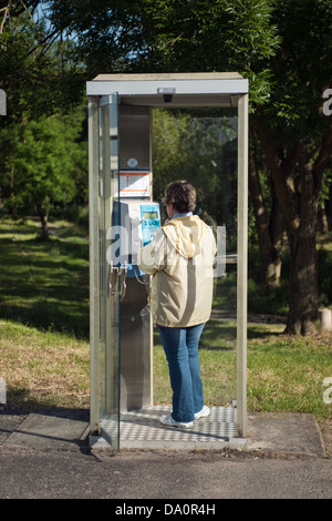 Una donna di mezza età usando un tipico francese telefono pubblico box in un ambiente rurale in Francia Foto Stock