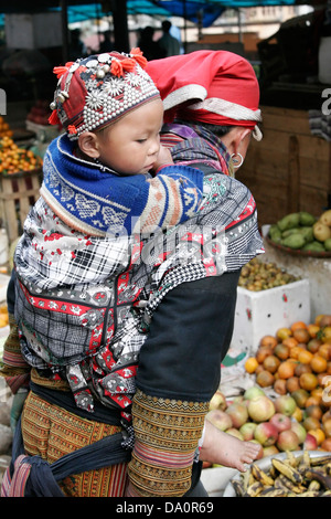 Giovani Red Dzao donna con il suo bambino sulla schiena nel regno vegetale e il mercato della frutta di Sapa, del Vietnam del nord, sud-est asiatico Foto Stock