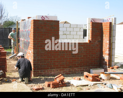 Builder / lavoratore edile lavorando su una parete di mattoni mattoni di cementazione per una nuova proprietà o estensione, apprendimento apprendista Foto Stock