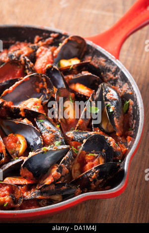 Cozze su stirfried salsa di pomodoro in un tegame rosso Foto Stock