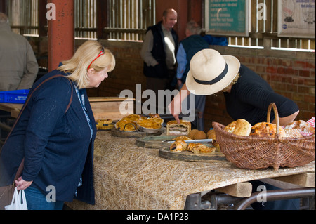 Donna che indossa hat vendendo torte sulla sua stallo a mensile del mercato degli agricoltori in Malton Ryedale North Yorkshire England Regno Unito Foto Stock