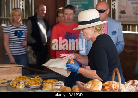 Donna che indossa hat vendendo torte sulla sua stallo a mensile del mercato degli agricoltori in Malton Ryedale North Yorkshire England Regno Unito Foto Stock