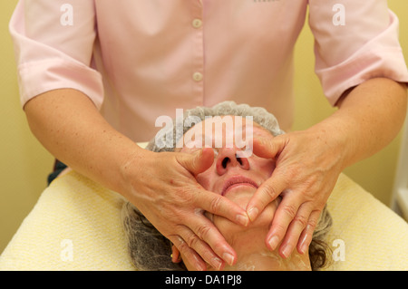 Donna di mezza età avente un massaggio viso alla clinica di bellezza Foto Stock