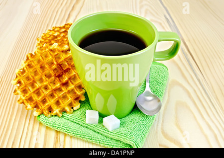 Due golden round waffle, verde mug, zucchero, cucchiaio sul tovagliolo verde su uno sfondo di legno Foto Stock
