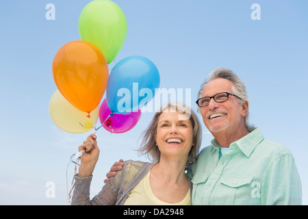 Coppia senior con grappolo di palloncini contro il cielo chiaro Foto Stock