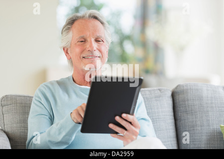 Senior uomo seduto sul divano con tavoletta digitale Foto Stock